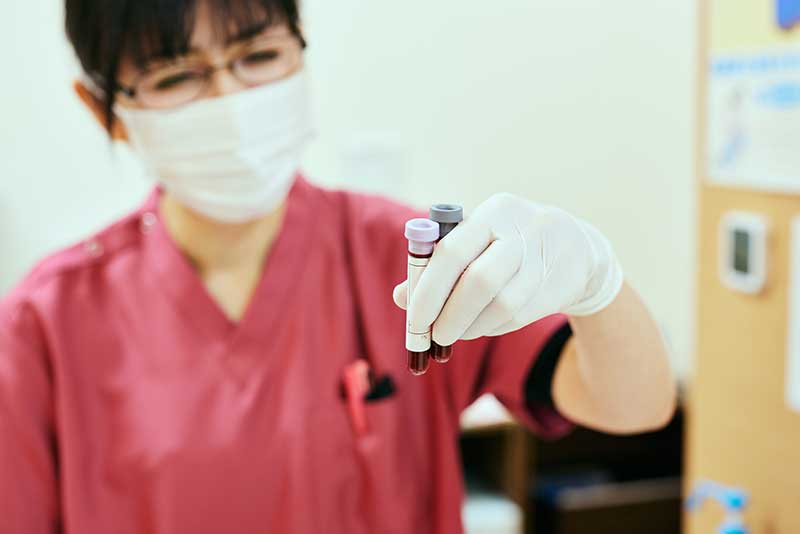 woman in scrubs and mask holding viles of blood