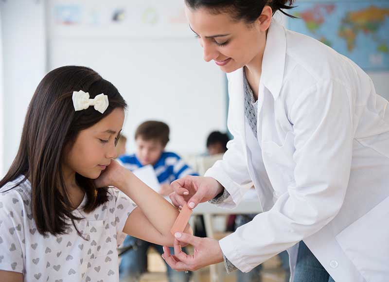 nurse in school giving child a band-aid